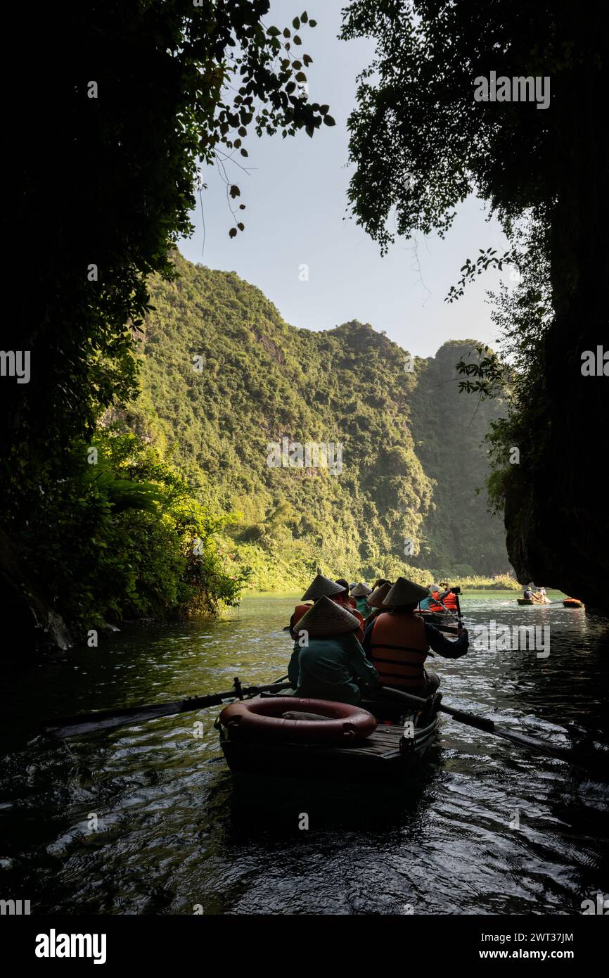 Small rowboats filled with tourists emerge from a cave on a river amid limestone mountains in Tam Coc, Ninh Binh province, northern Vietnam. Stock Photo