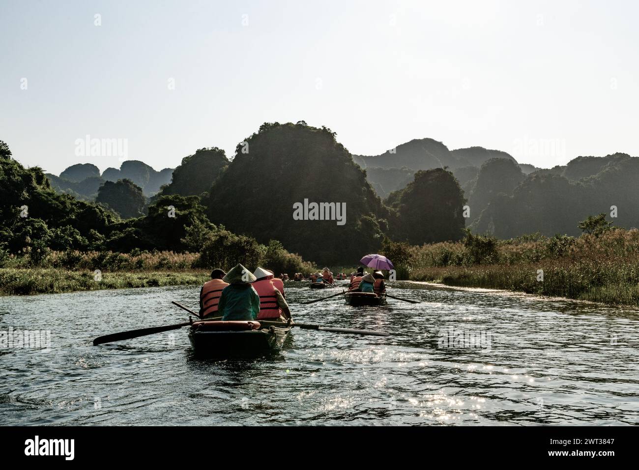 Small rowboats filled with tourists float down a river amid limestone mountains in Tam Coc, Ninh Binh province, northern Vietnam. Stock Photo
