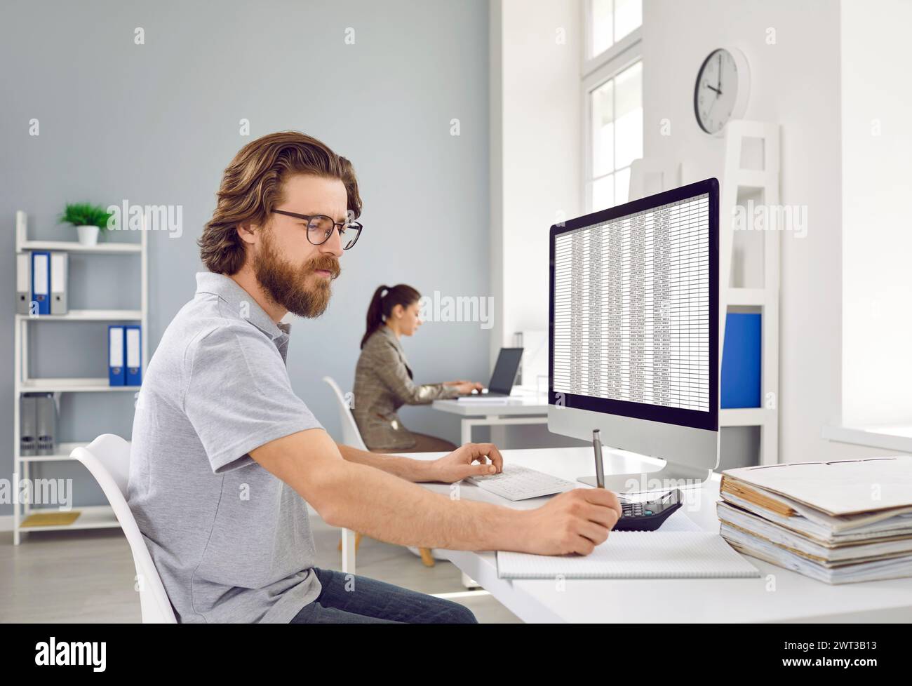 Serious man is focused on work with accounting program on computer and paper records. Stock Photo