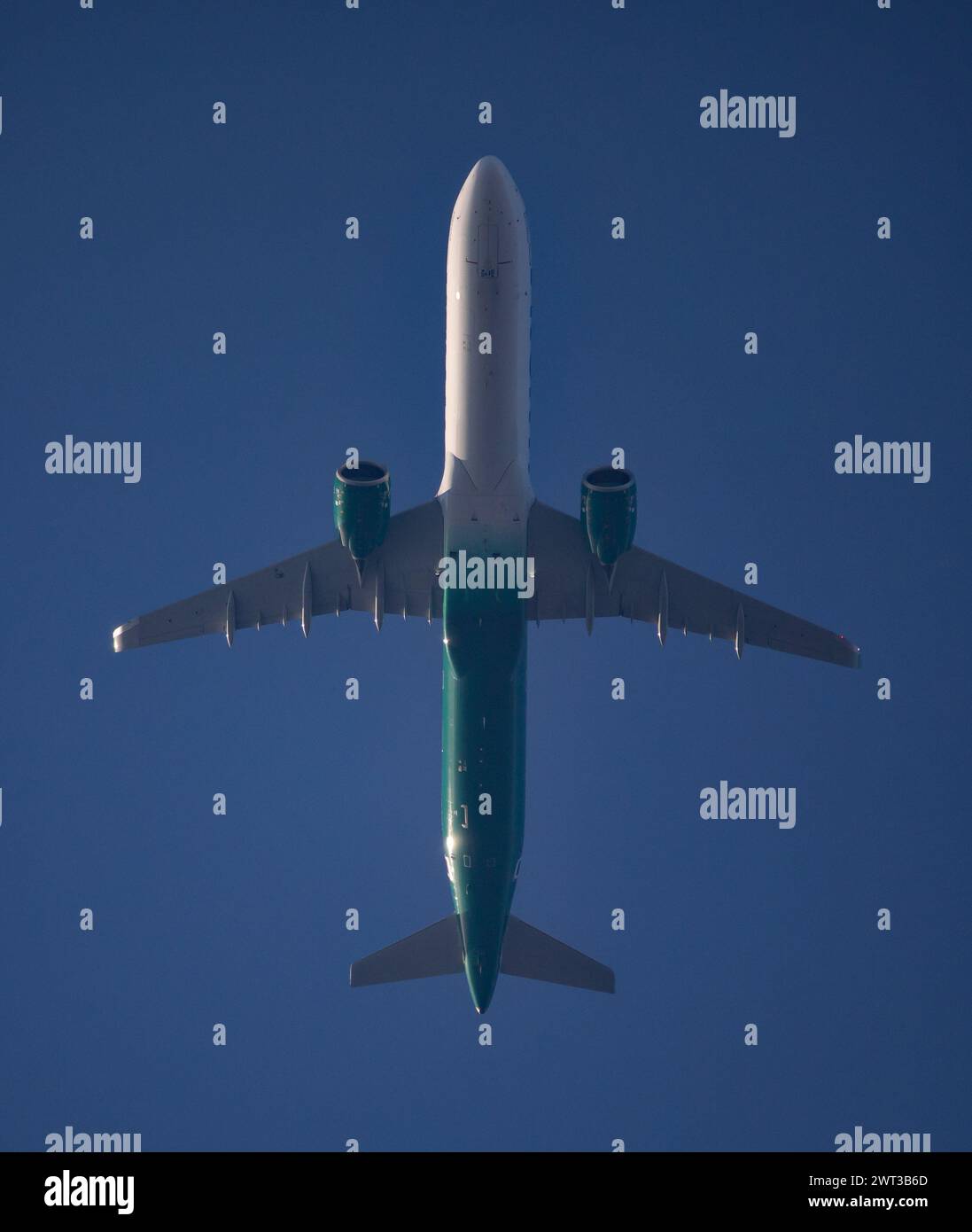 A commercial airliner passes directly overhead in a deep blue sky at ...