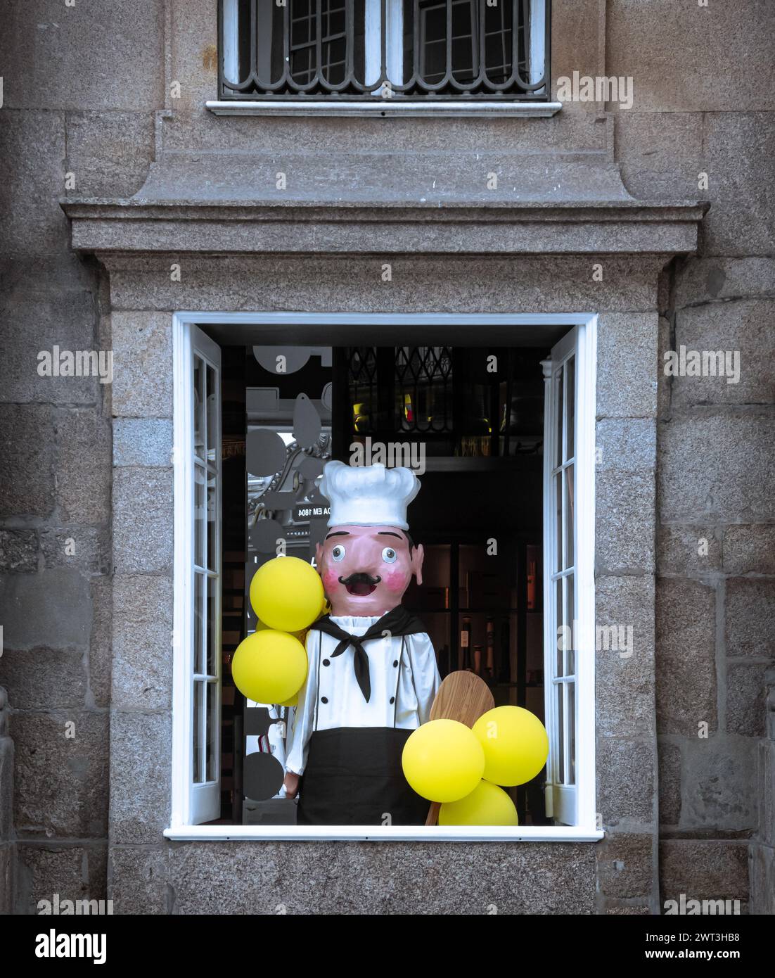 Life size puppet of traditional chef holding balloons in open large window in stone building Stock Photo