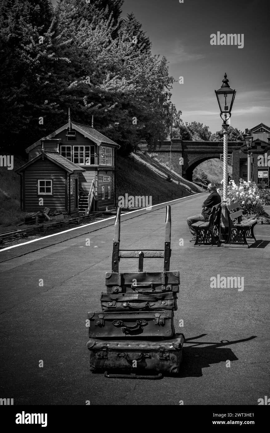 Vintage steam railway station platform with old luggage on barrow and one person waiting for train Stock Photo