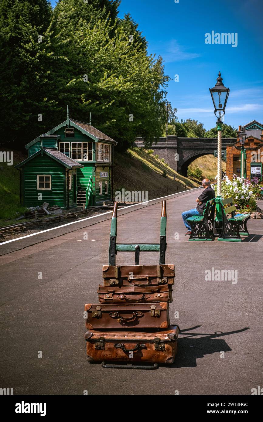 Vintage steam railway station platform with old luggage on barrow and one person waiting for train Stock Photo