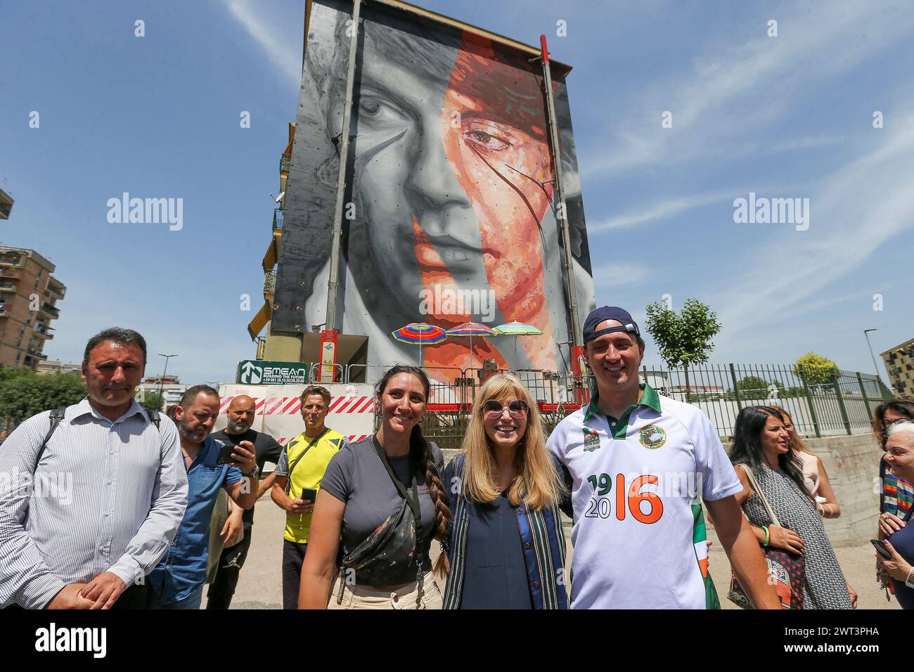 The artists Jorit (right), Dori Ghezzi (center), and Trisha (left) in front of the mural depicting the famous Italian singer-songwriter Fabrizio De An Stock Photo