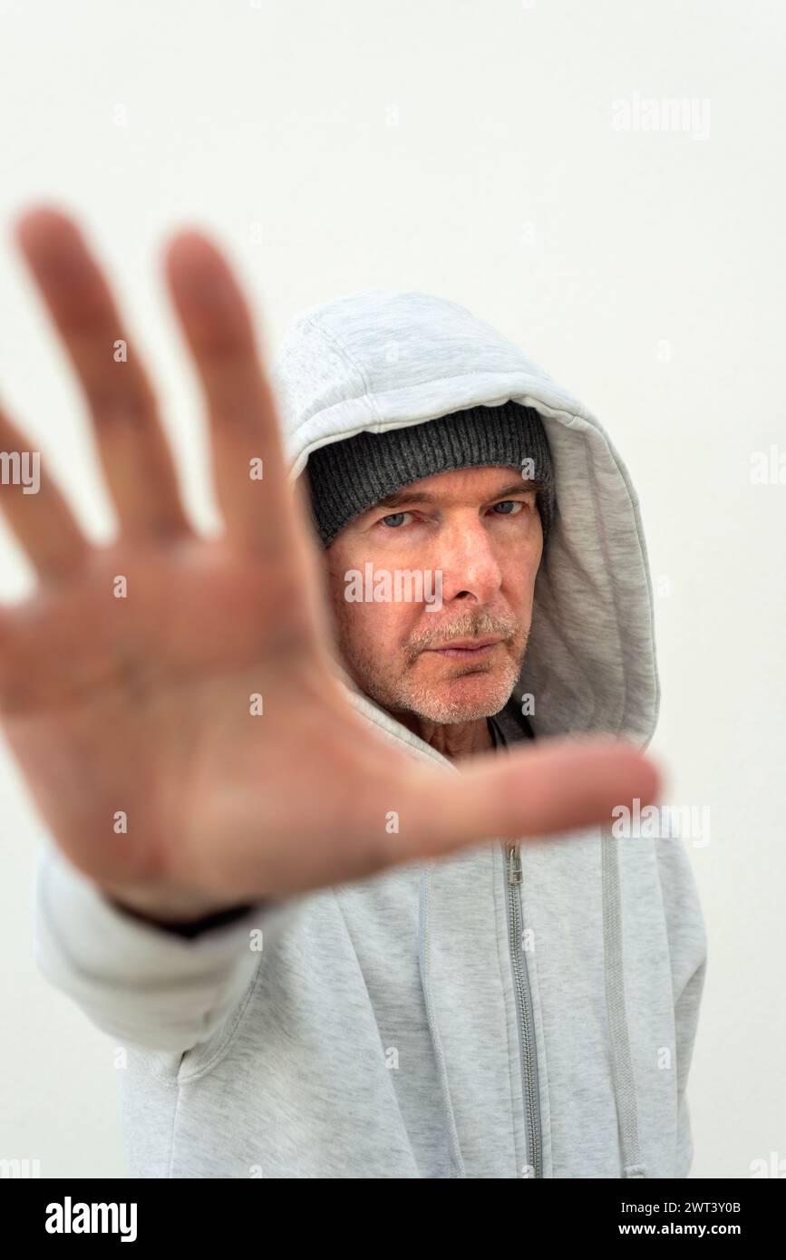 Portrait of a mid adult man wearing a hoodie with his hand up, stop. Stock Photo