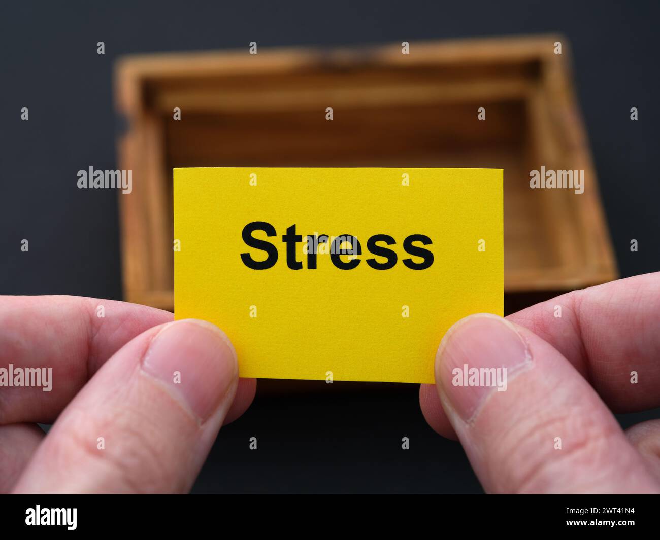 A man holding a piece of yellow paper with the word Stress on it in his hands over a small empty wooden box. Close up. Stock Photo