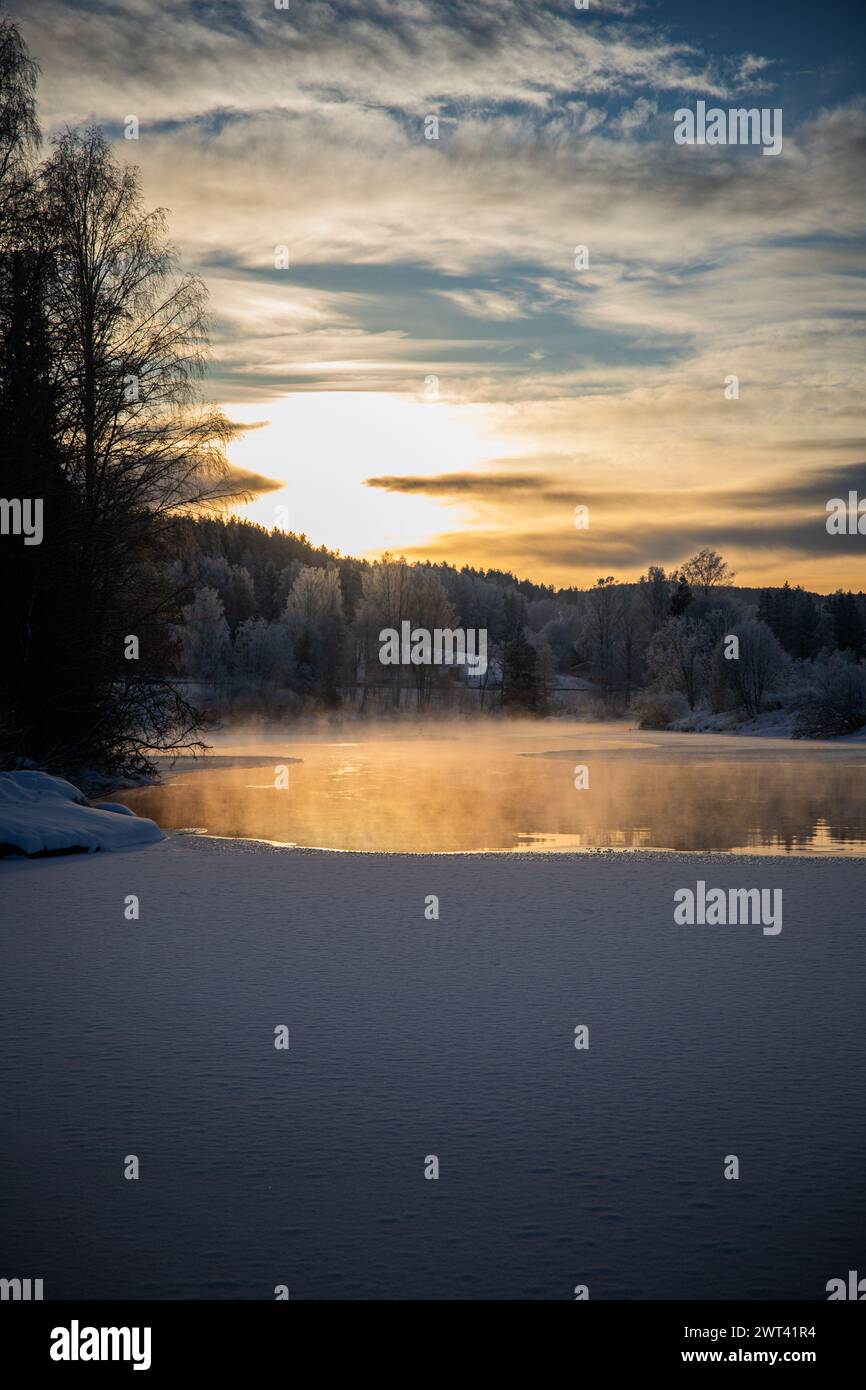 A sunset over snow-covered lake with trees, tranquil winter scene Stock Photo
