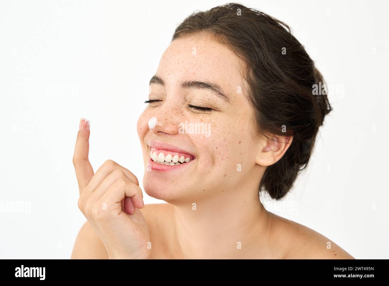 Happy Latin young woman freckled face applying cream on nose isolated on white. Stock Photo
