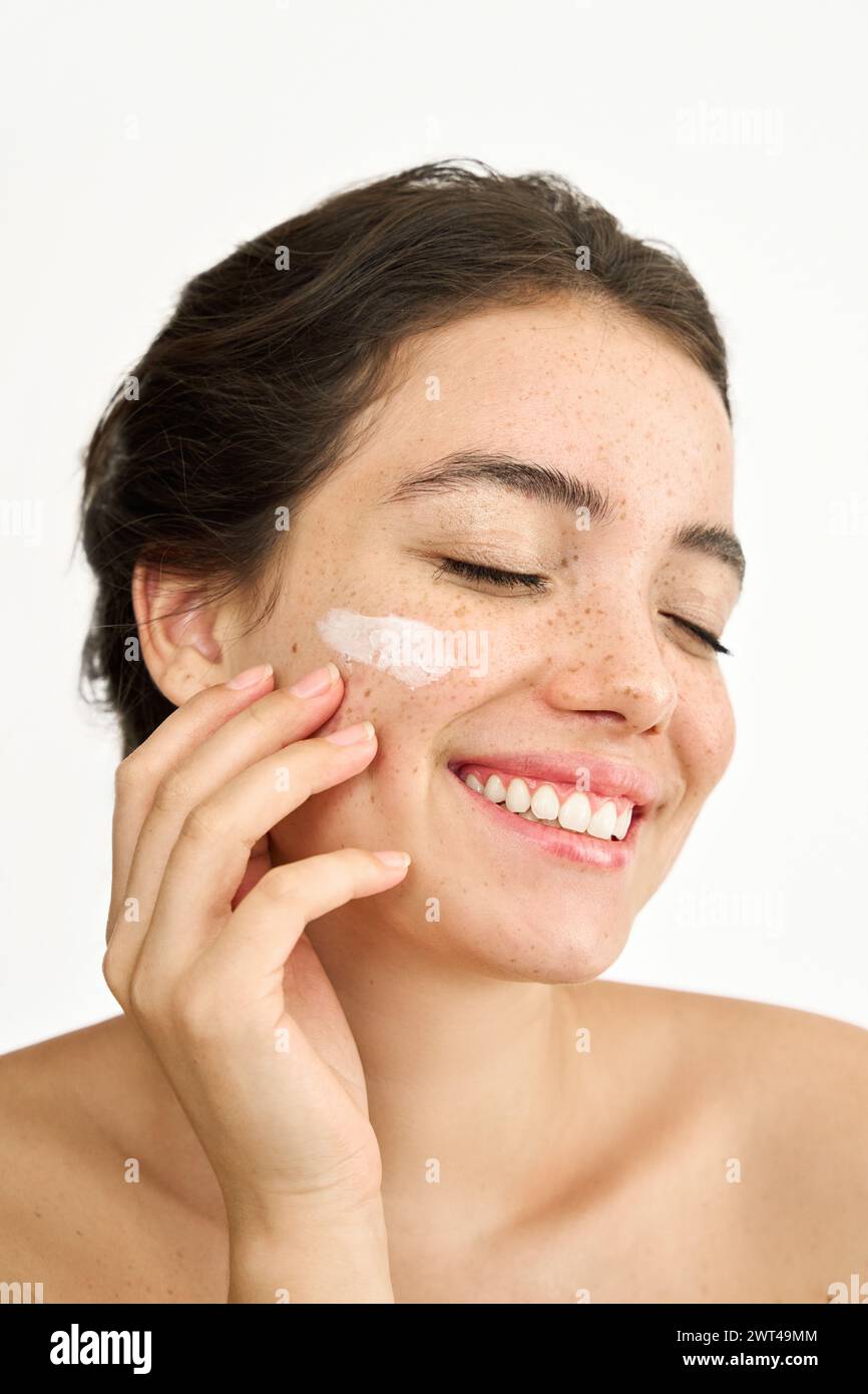 Happy Latin young woman applying face cream isolated on white, vertical. Stock Photo