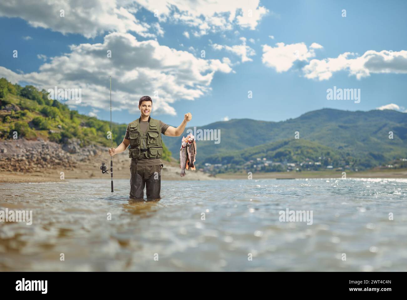 Young fisherman posing with a fishing rod and fish inside a lake Stock Photo