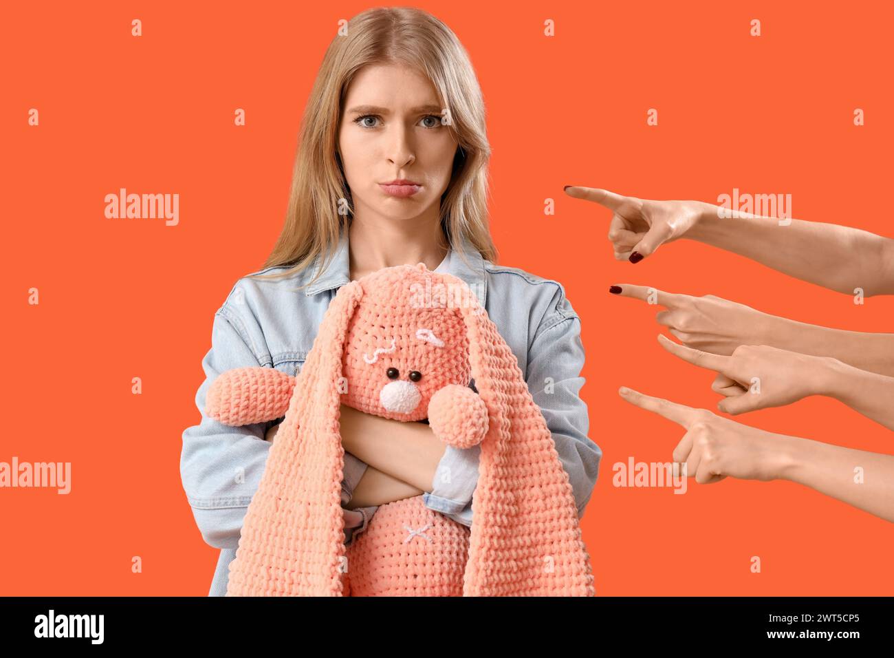 People pointing at upset young woman with toy on orange background. Accusation concept Stock Photo