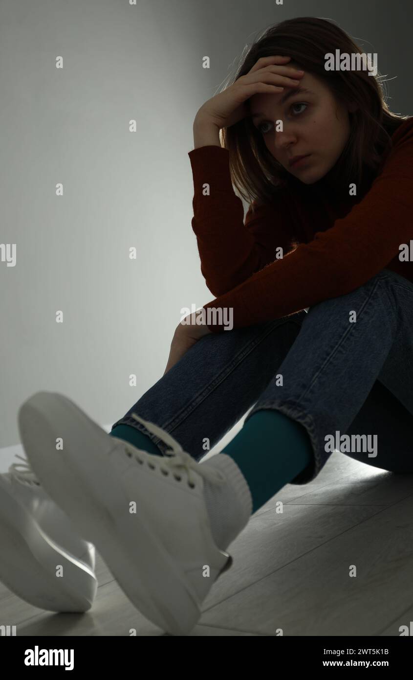 Sad young woman sitting on floor near grey wall indoors Stock Photo - Alamy