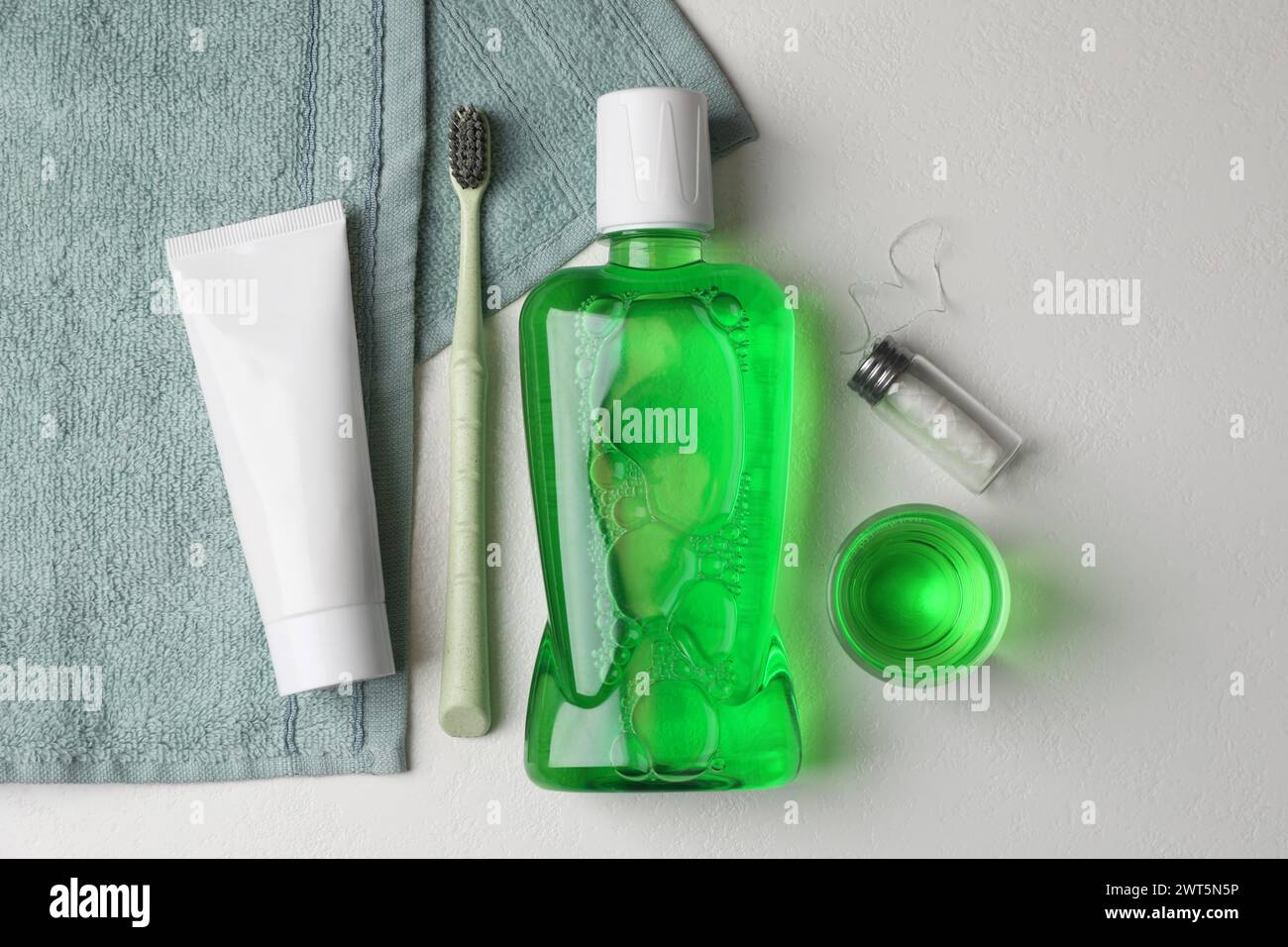 Fresh mouthwash in bottle, glass, toothbrush, toothpaste and dental floss on light background, flat lay Stock Photo