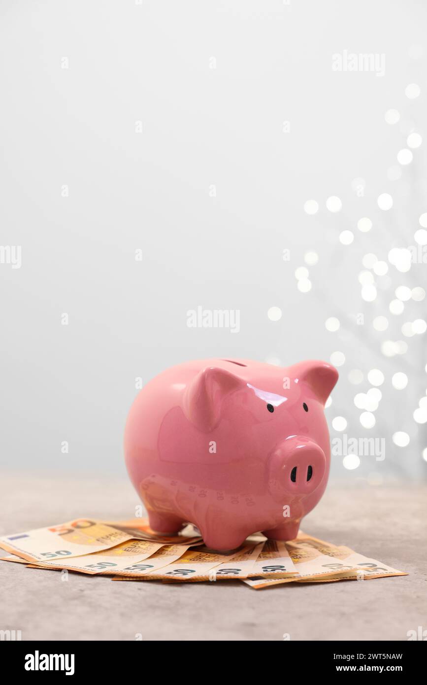 Piggy bank with euro banknotes on grey table against blurred lights ...