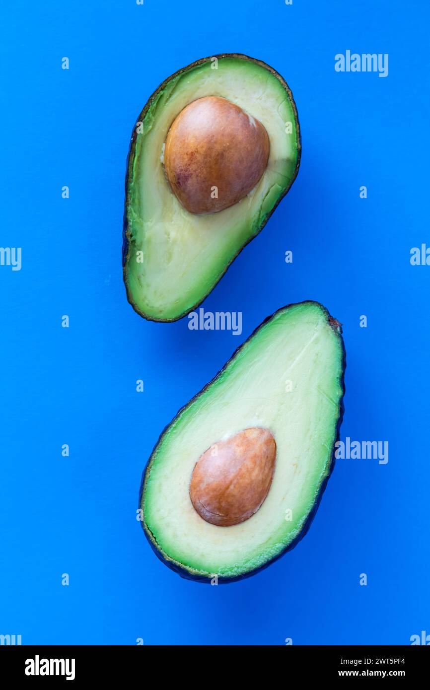 Cut avocados with the seed in the middle, against a bright blue background Stock Photo