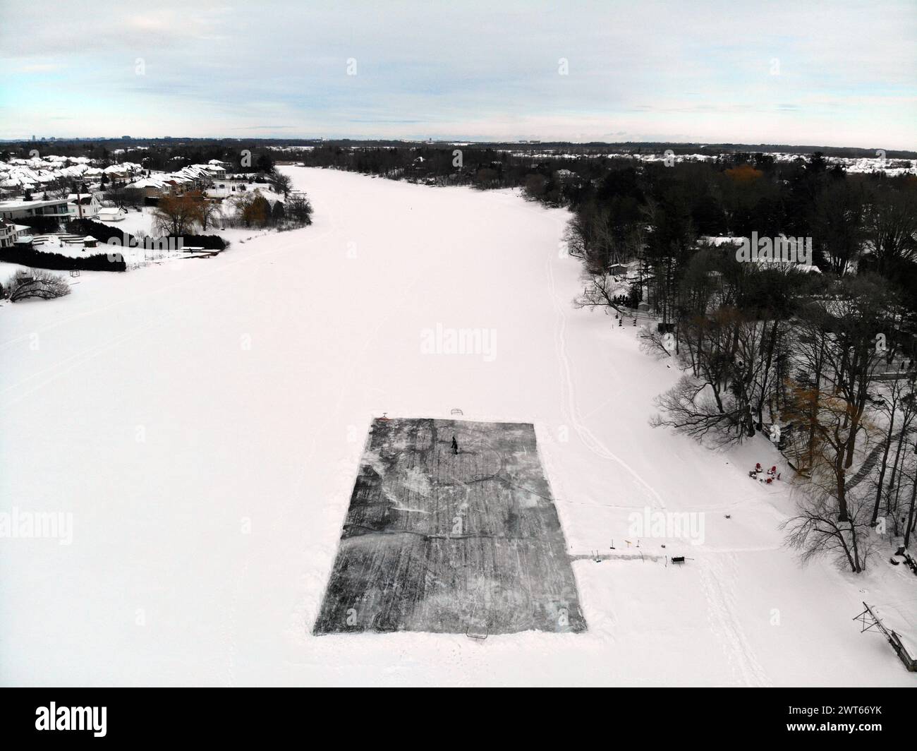 Rideau River covered by ice and snow with a skating rink cleared for hockey, under cloudy skies and with tree-lined river banks Stock Photo