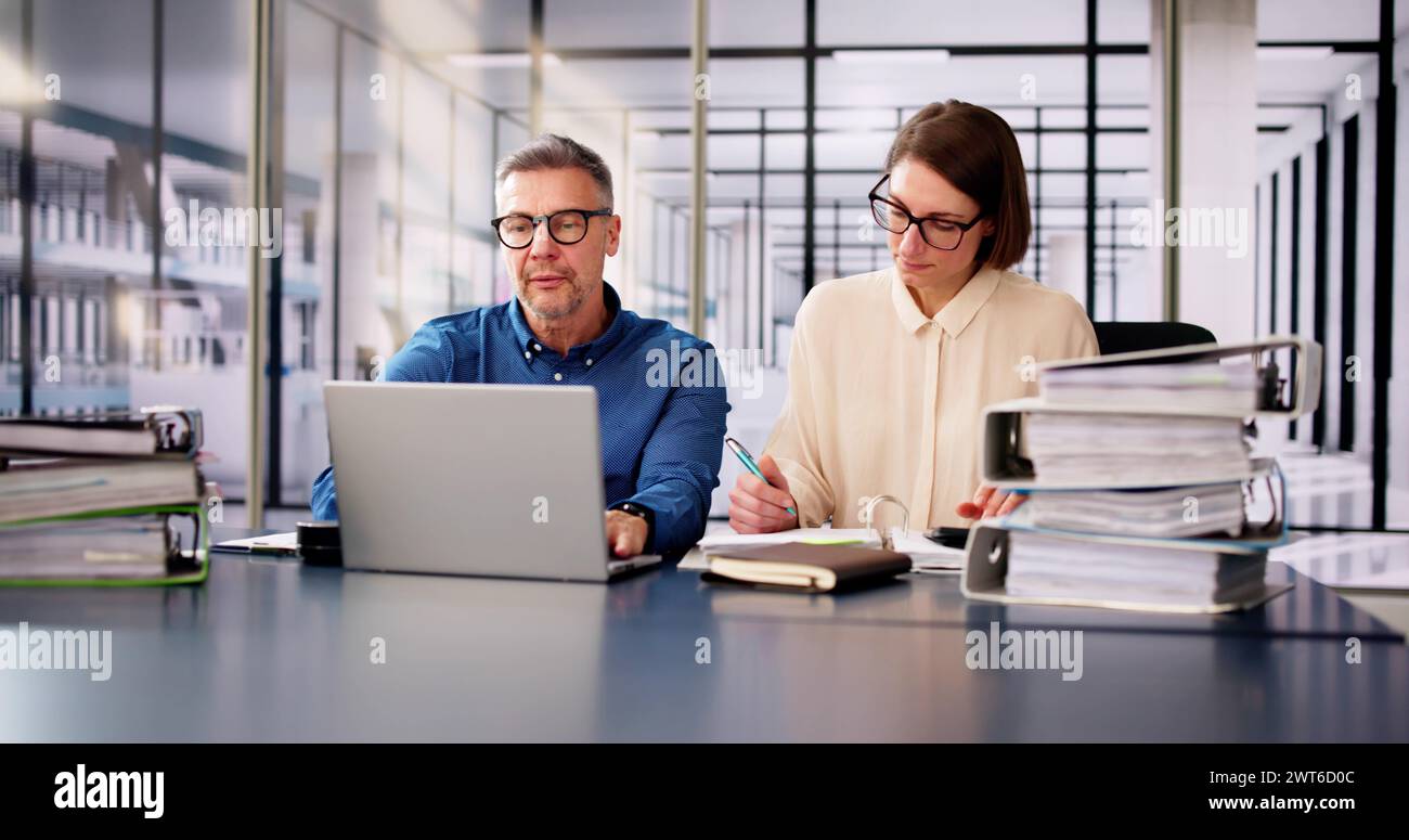 Two Businesspeople Calculating Invoice In Office While Using Laptop Stock Photo