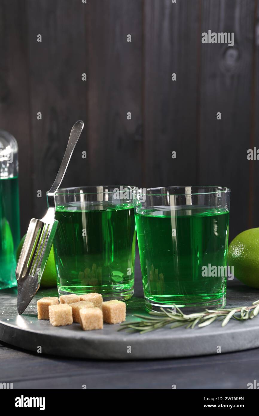 Absinthe in glasses, rosemary, brown sugar and spoon on table. Alcoholic drink Stock Photo