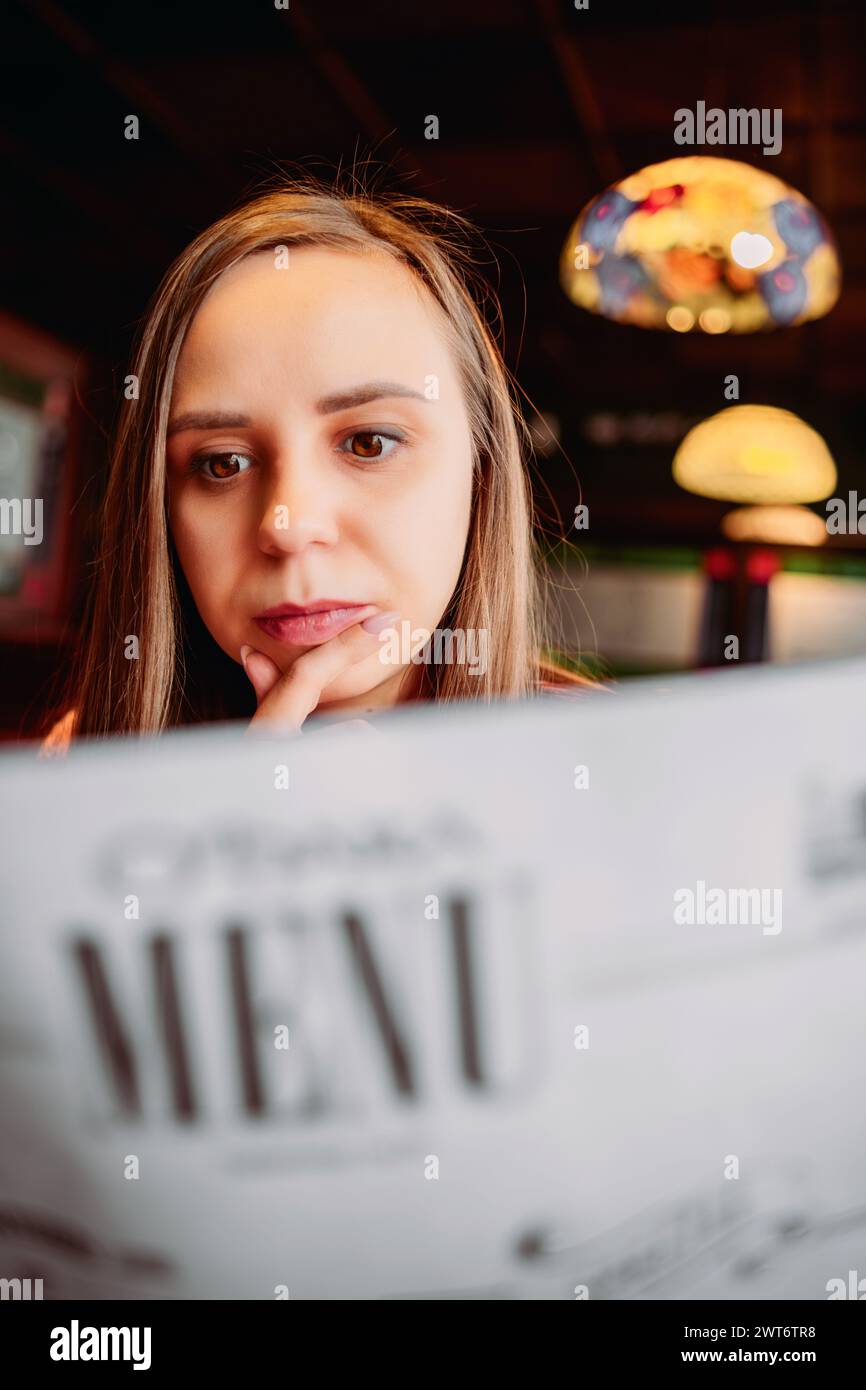 A woman is seated at a table, attentively reading a menu Stock Photo