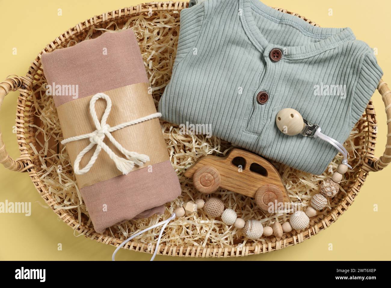 Different baby accessories and clothes in wicker basket on yellow background, top view Stock Photo