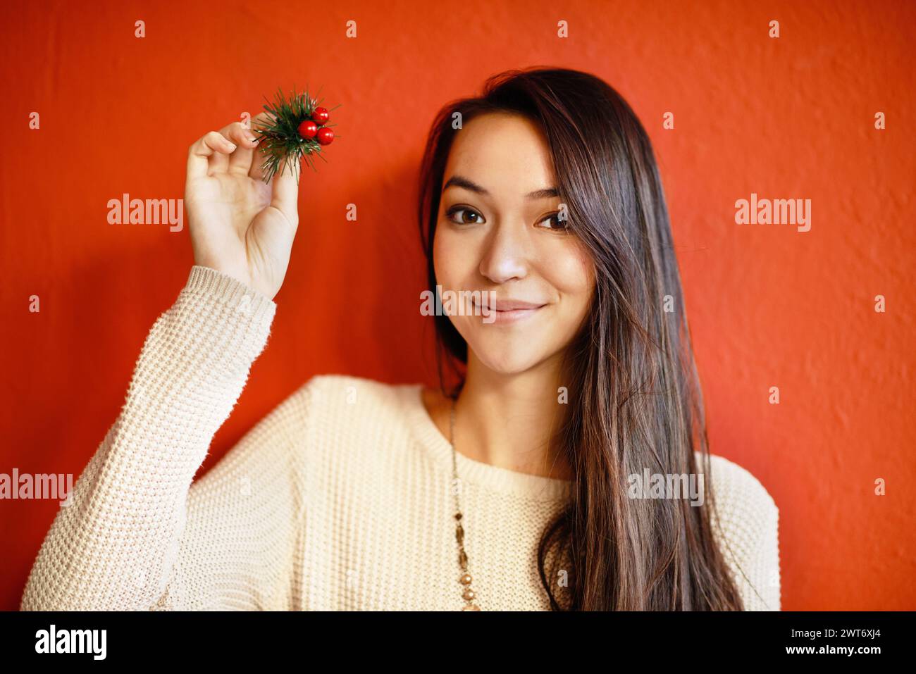 Christmas, portrait and happy woman with holly branch in hand and winter celebration by red background. Young, person and smile on face with holiday Stock Photo