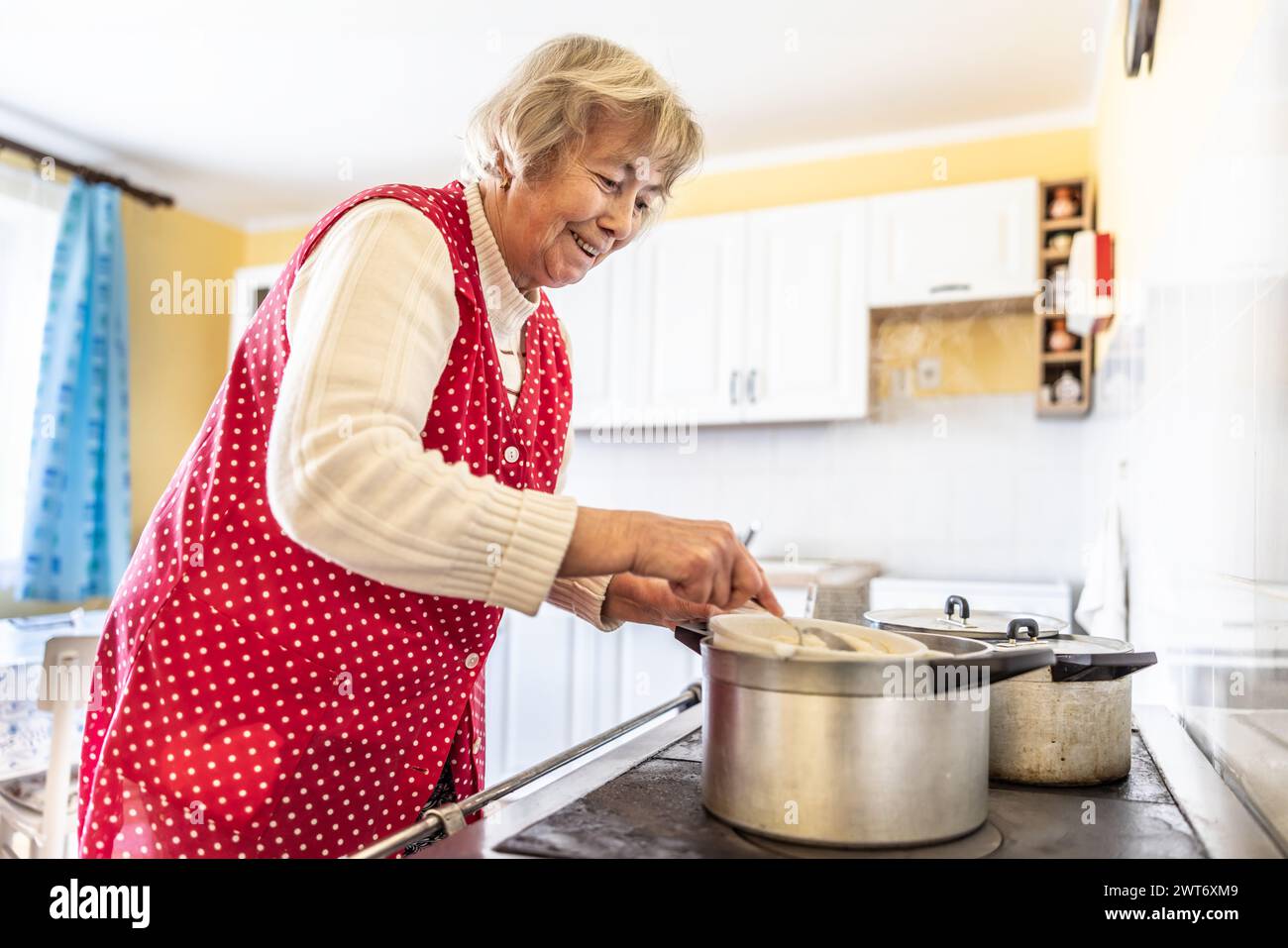 Grandma cooks bryndzove halusky, a traditional Slovak dish, on her old oven. A pensioner cooks food in her kitchen. Stock Photo