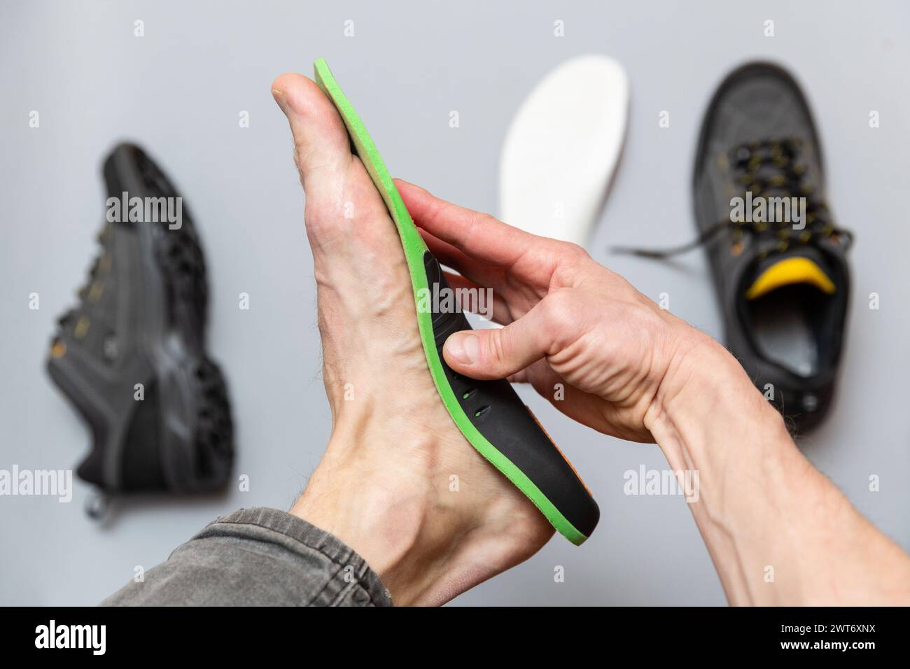 Close up of man hands fitting orthopedic insoles on a gray background. Healthcare and orthopedic treatment and prevention of flatfeet concept. Stock Photo