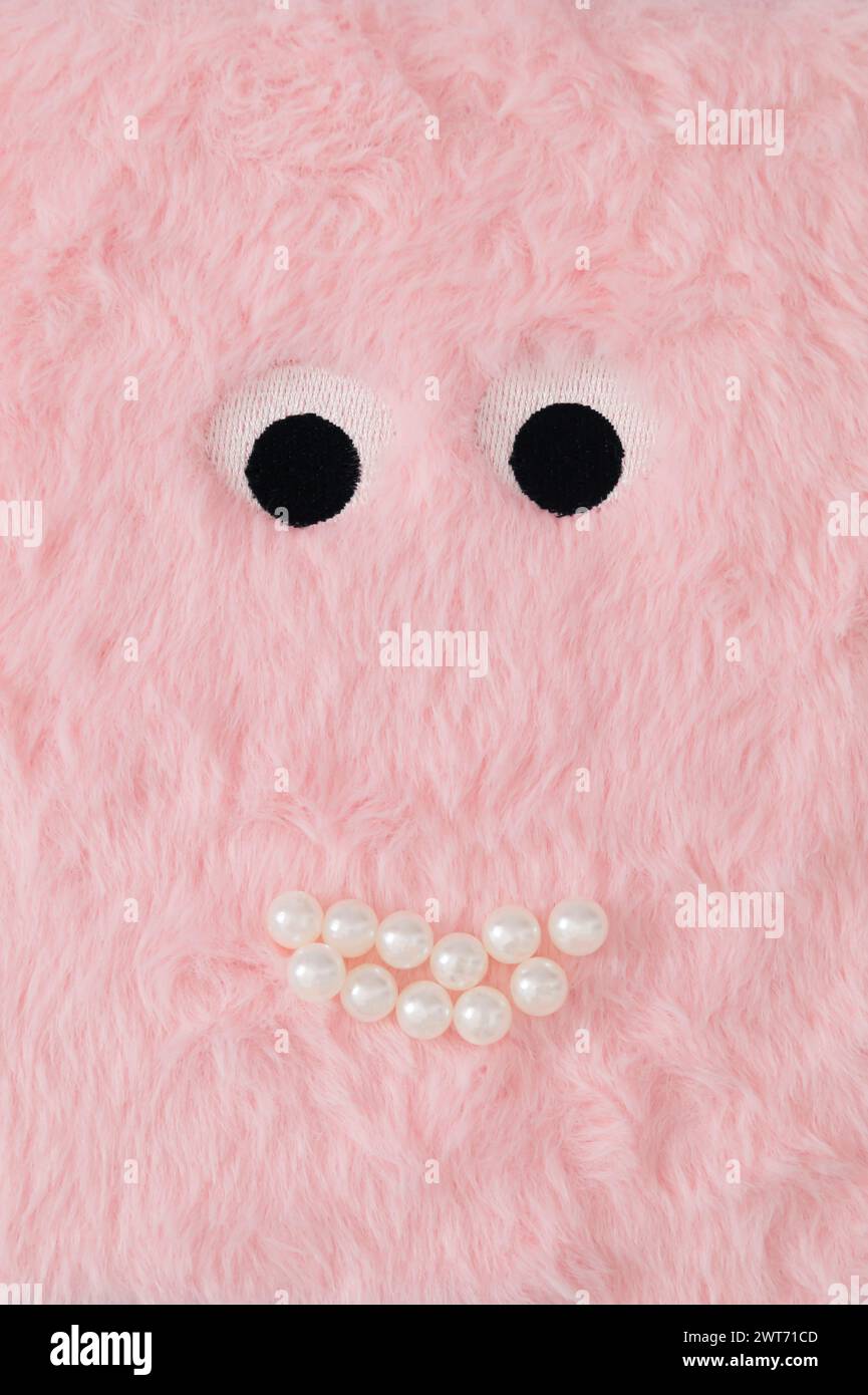 Cute fluffy monster made with pastel pink faux fur and white pearls. Minimal concept. Creative funny face composition. An original cute fluffy monster Stock Photo