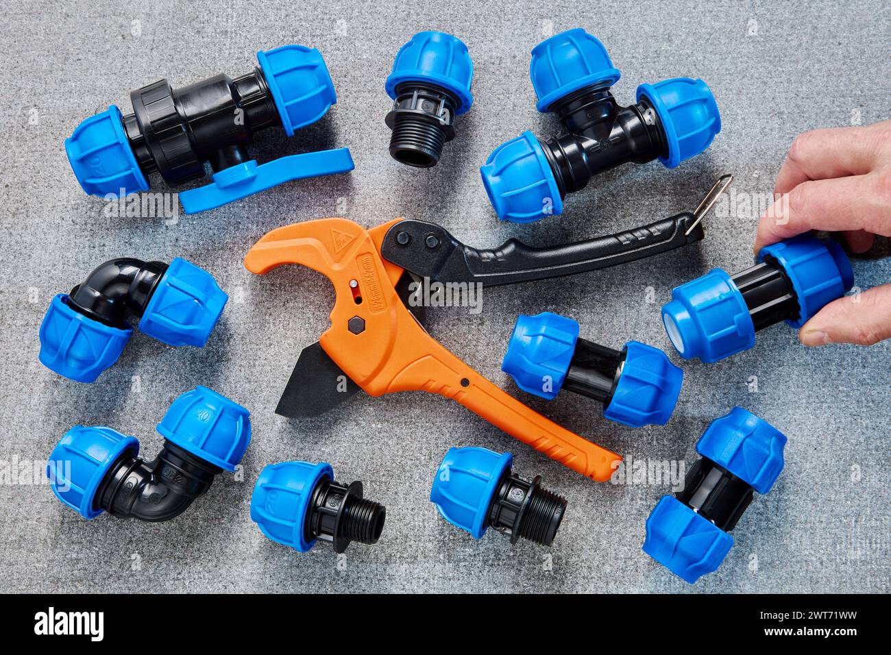 Assorted Blue Polyethylene Pipe Fittings and an Orange PVC Pipe Cutter on a Grey Background
