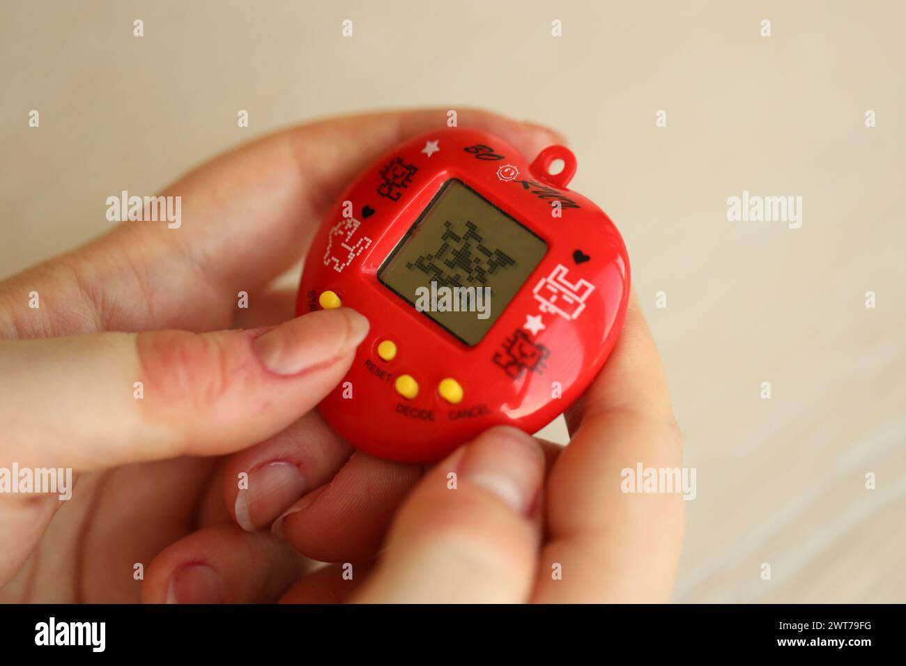 KYIV, UKRAINE - MARCH 9, 2024 Retro pet keychain game tamagotchi in red plastic case in female hands close up Stock Photo