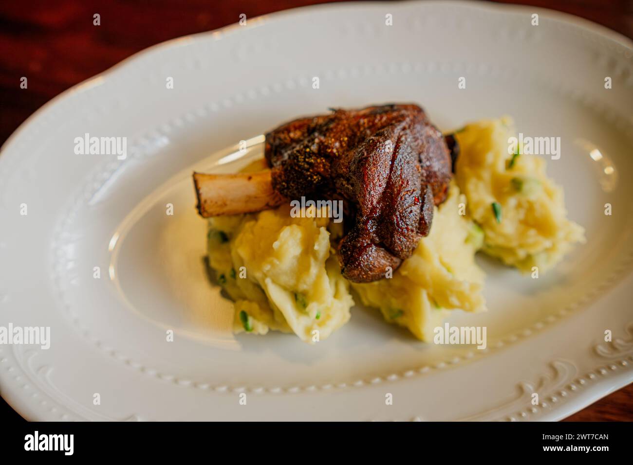 Succulent Baked Lamb Shank Served Atop Creamy Mashed Potatoes on a White Plate. Stock Photo