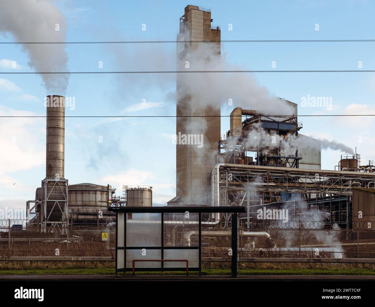 Bus stop in front of fertiliser plant and ICI tower in Stockton-on-tees. Chimneys bellow out steam and large industrial pipes in the background. UK Stock Photo