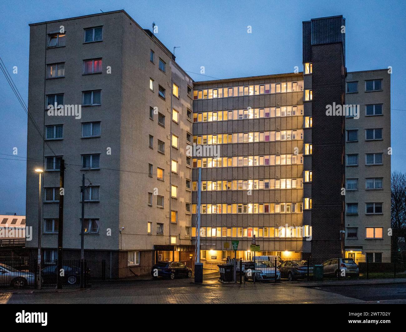 Residential 9-storey council flats at dusk. Lighting can be seen in the ...