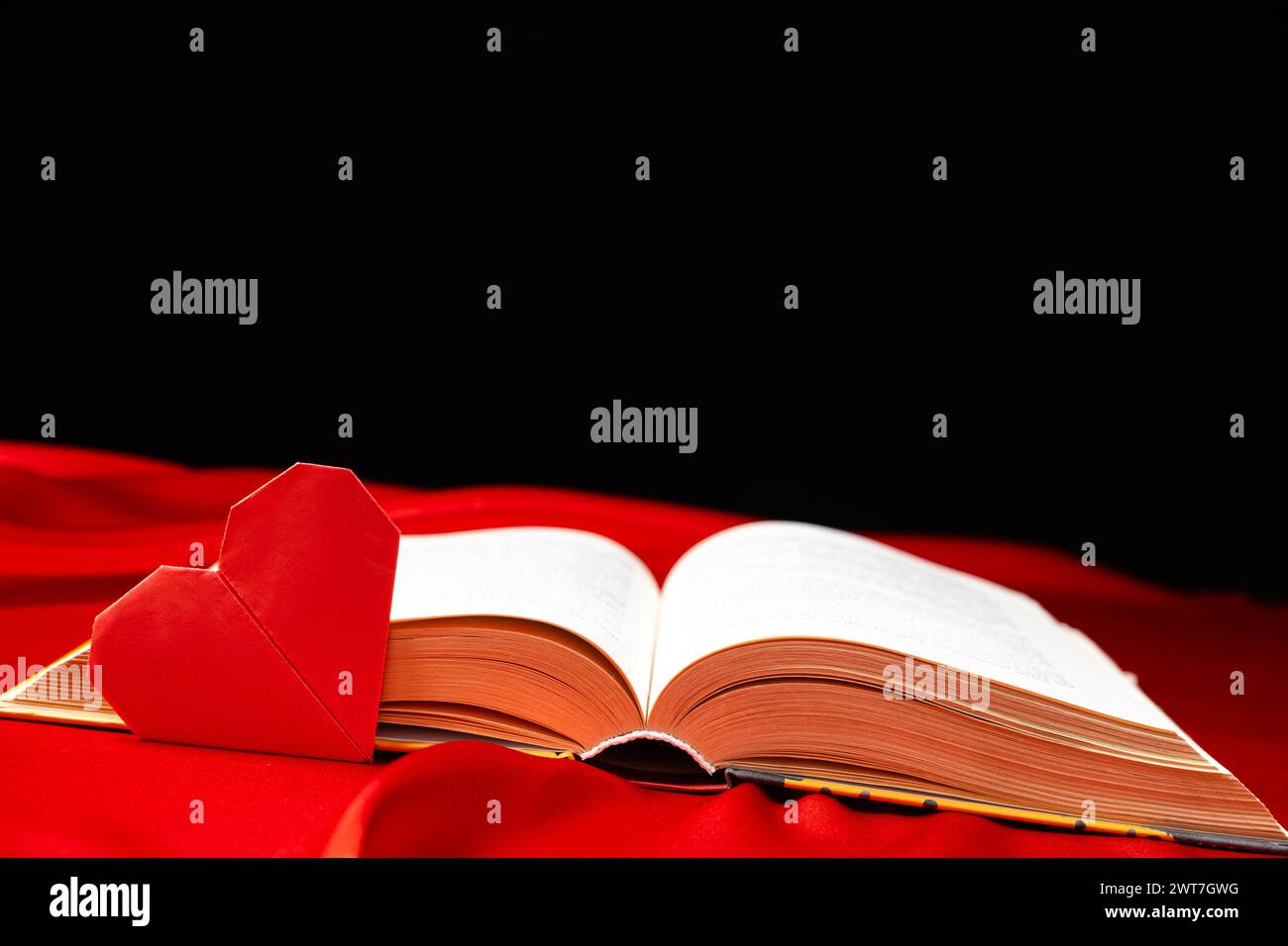 Origami paper heart and thick book on red and black background. Love for books. Stock Photo
