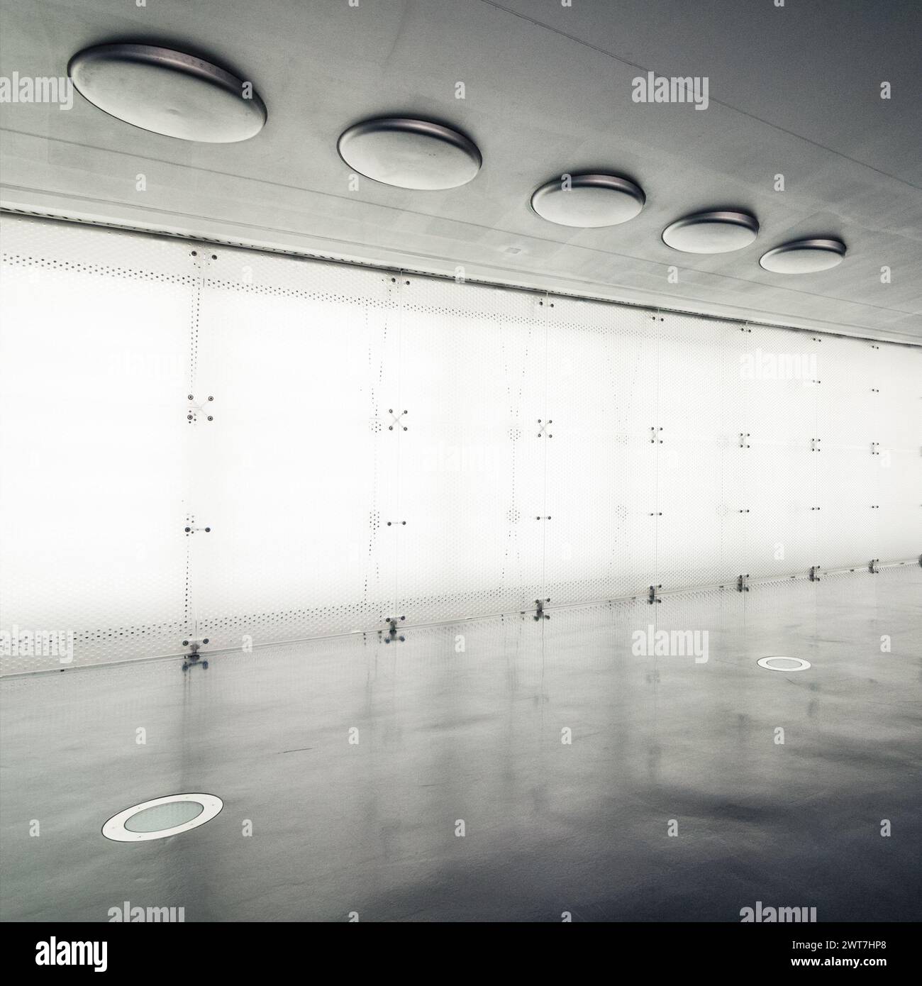Empty room illuminated wall and silver-colored ceiling. The floor is grey and ceiling has round portholes in it. Empty retrofuturistic interior. Stock Photo