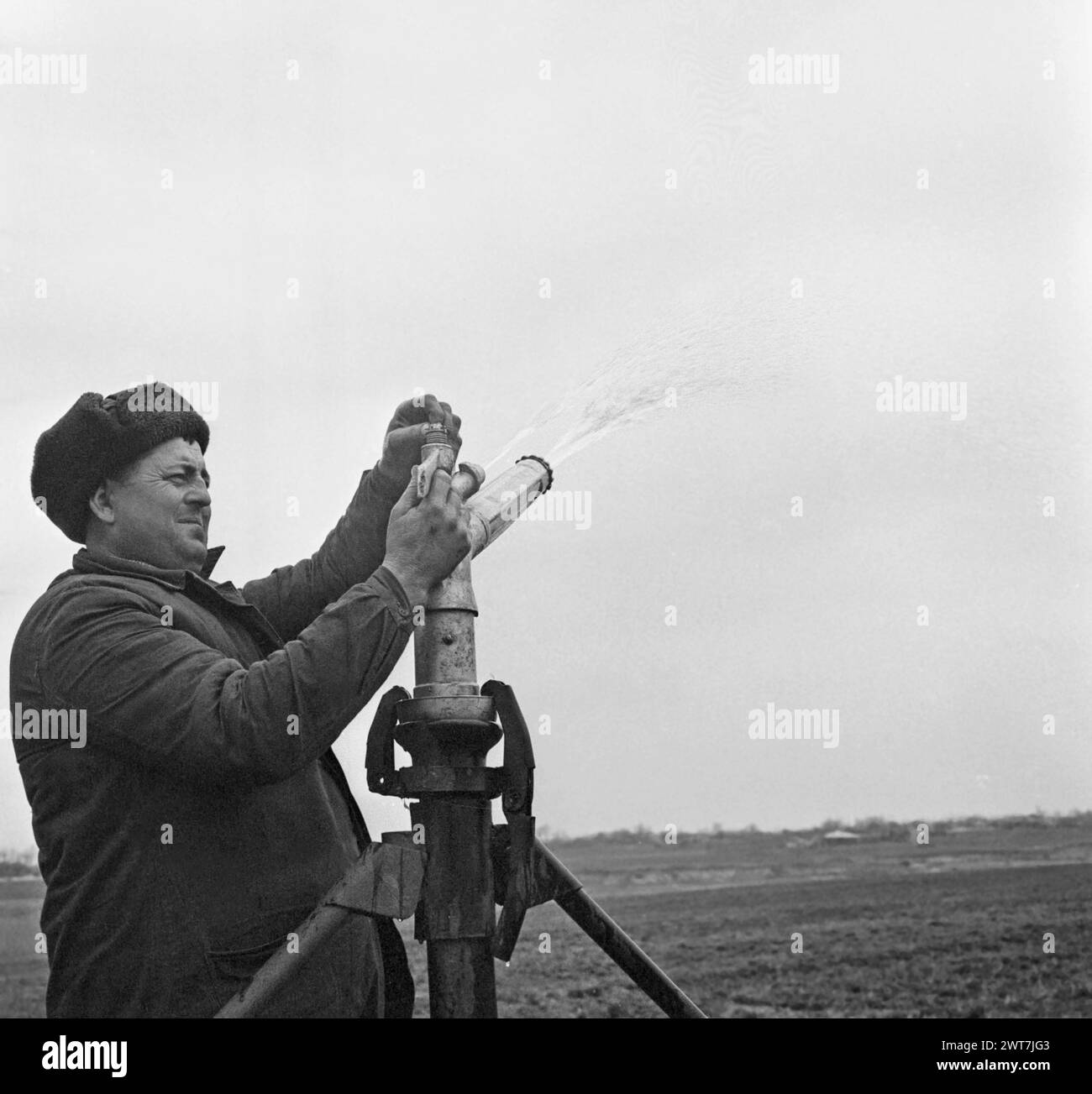 State agricultural cooperative in communist Romania, in the 1970s. Workers turning on the sprinklers. Stock Photo