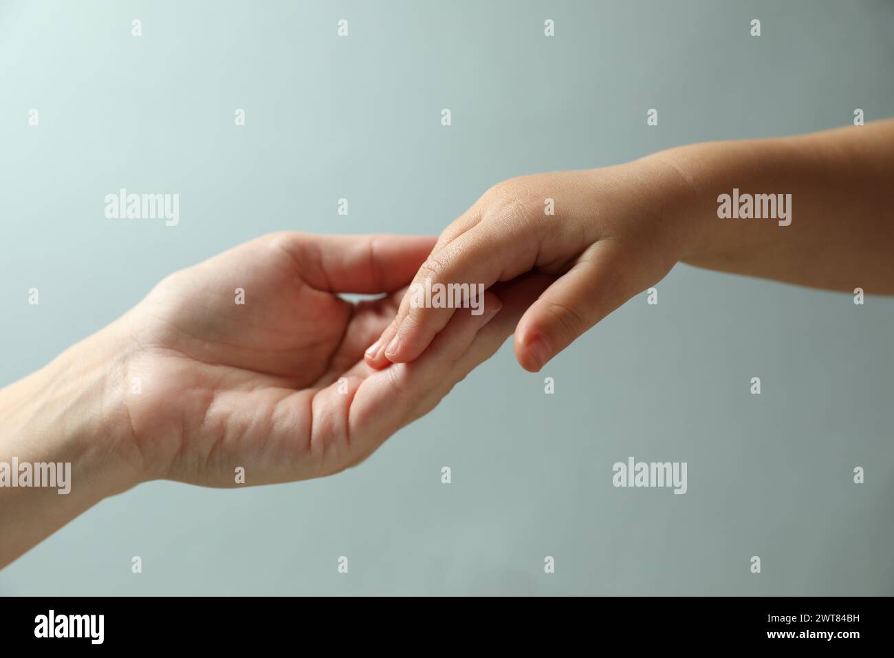Mother and child holding hands on light blue background, closeup Stock ...
