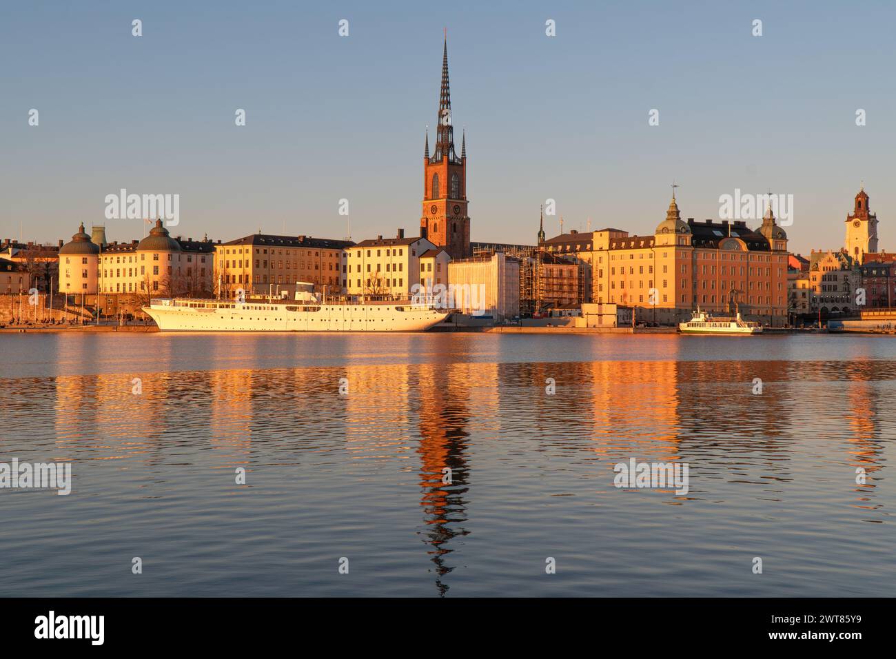 Riddarholmen church reflection in the lake at sunset. Stockholm, Sweden. Blue sky, late winter. Yellow buildings. Stock Photo