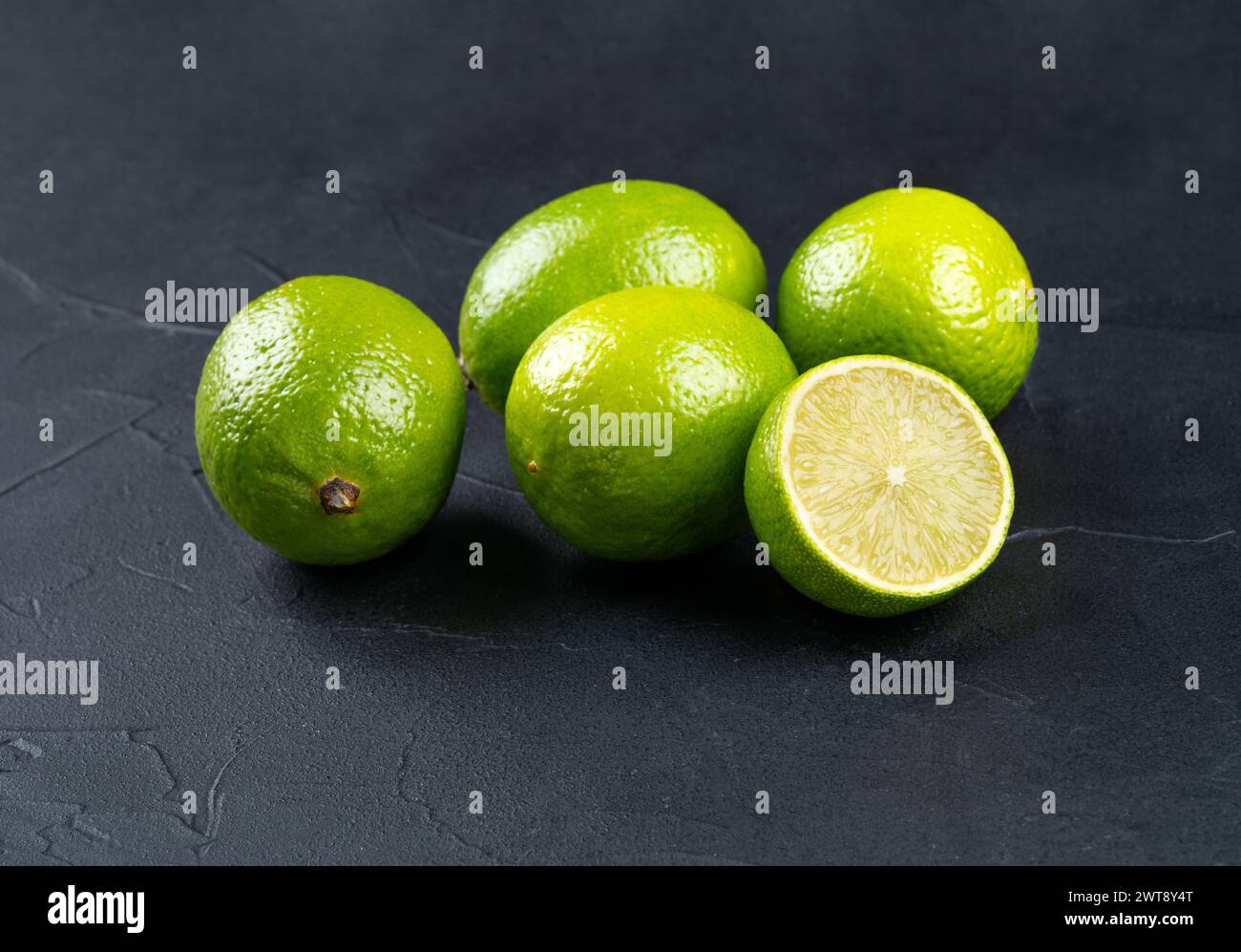 Several fresh lime fruits with a juicy half on a dark background Stock Photo