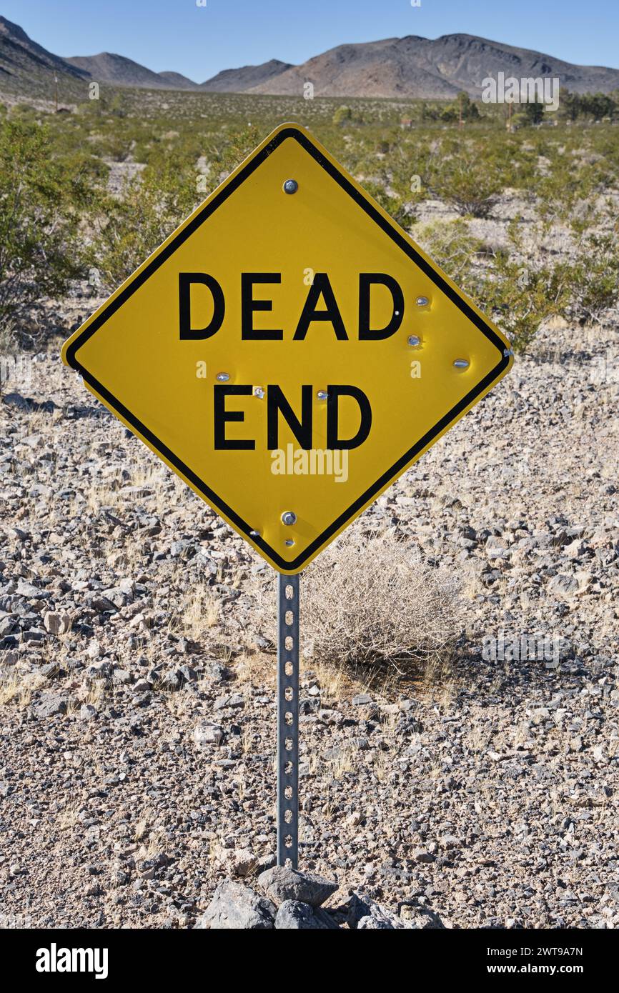 yellow and black dead end road sign in the desert with bullet holes ...