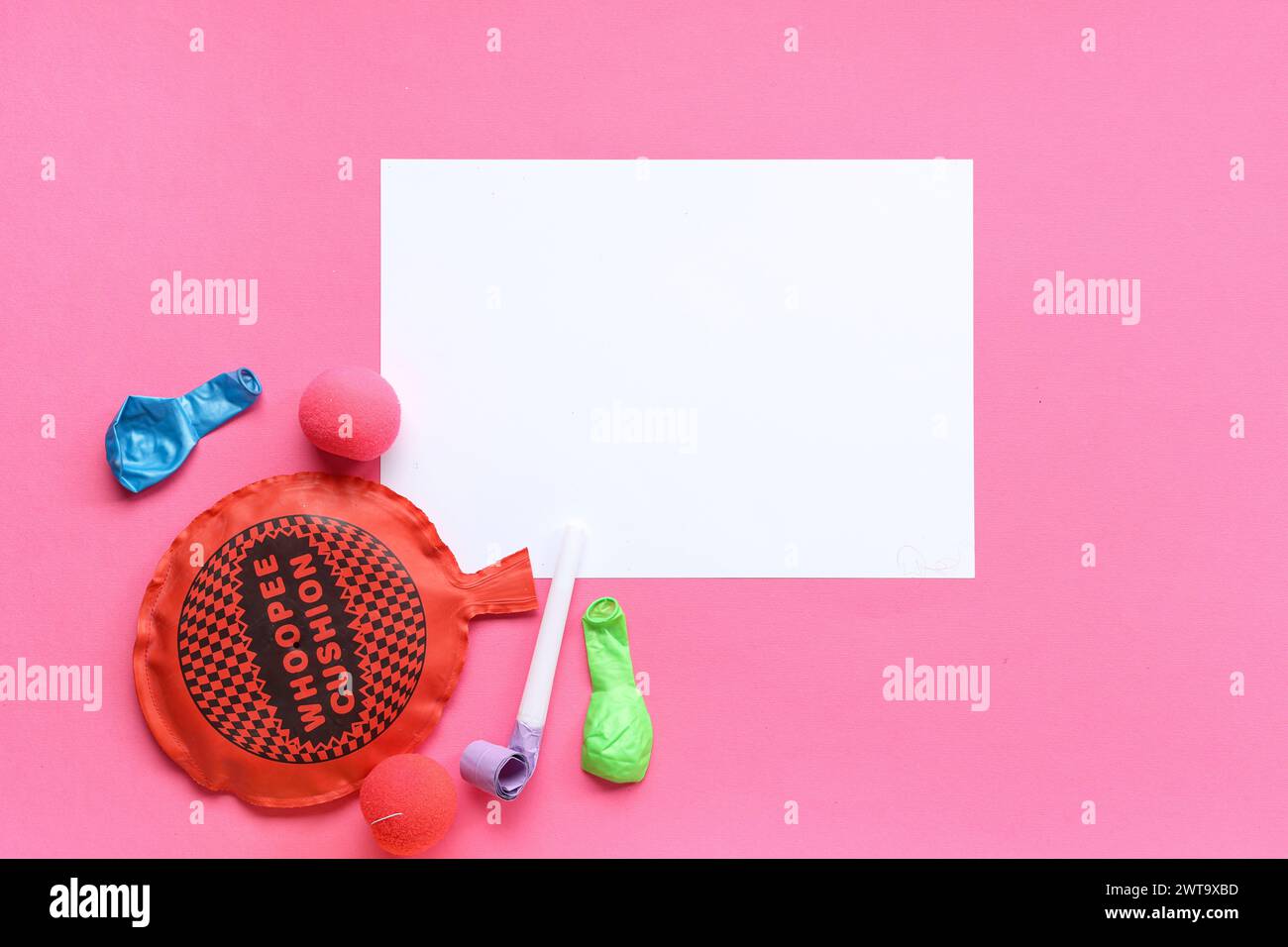 Blank card with whoopee cushion and party decor on pink background. April Fools Day celebration Stock Photo