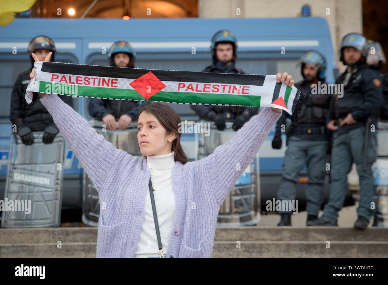 Rome, Italy. 16th Mar, 2024. A girl shows a scarf with the colors of the Palestinian flag and the writing 'Palestine' in front of the policemen lined up in riot gear in front of the Ministry of Education at the end of the 'Stop the genocide of the Palestinian people' demonstration march organized by the Palestinian Students Movement in Italy after the start of the holy month of Ramadan, and in which people of all political faiths participated, in Rome.The march ended in front of the headquarters of the Ministry of Education, in front of a large line of police in anti-riot gear, to contest the Stock Photo