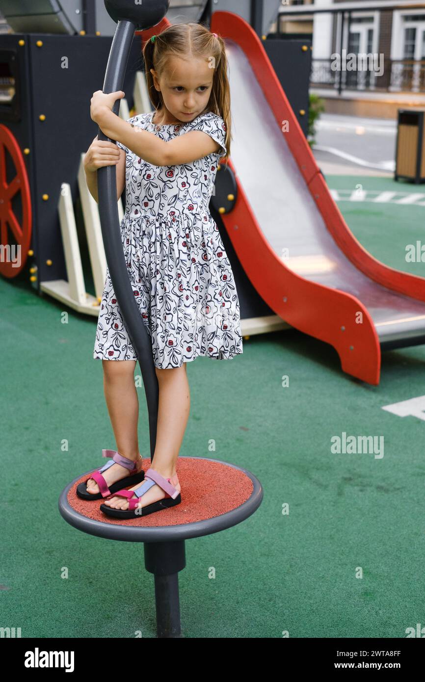 Child playing on playground in the city. Girl spinning and balancing ...