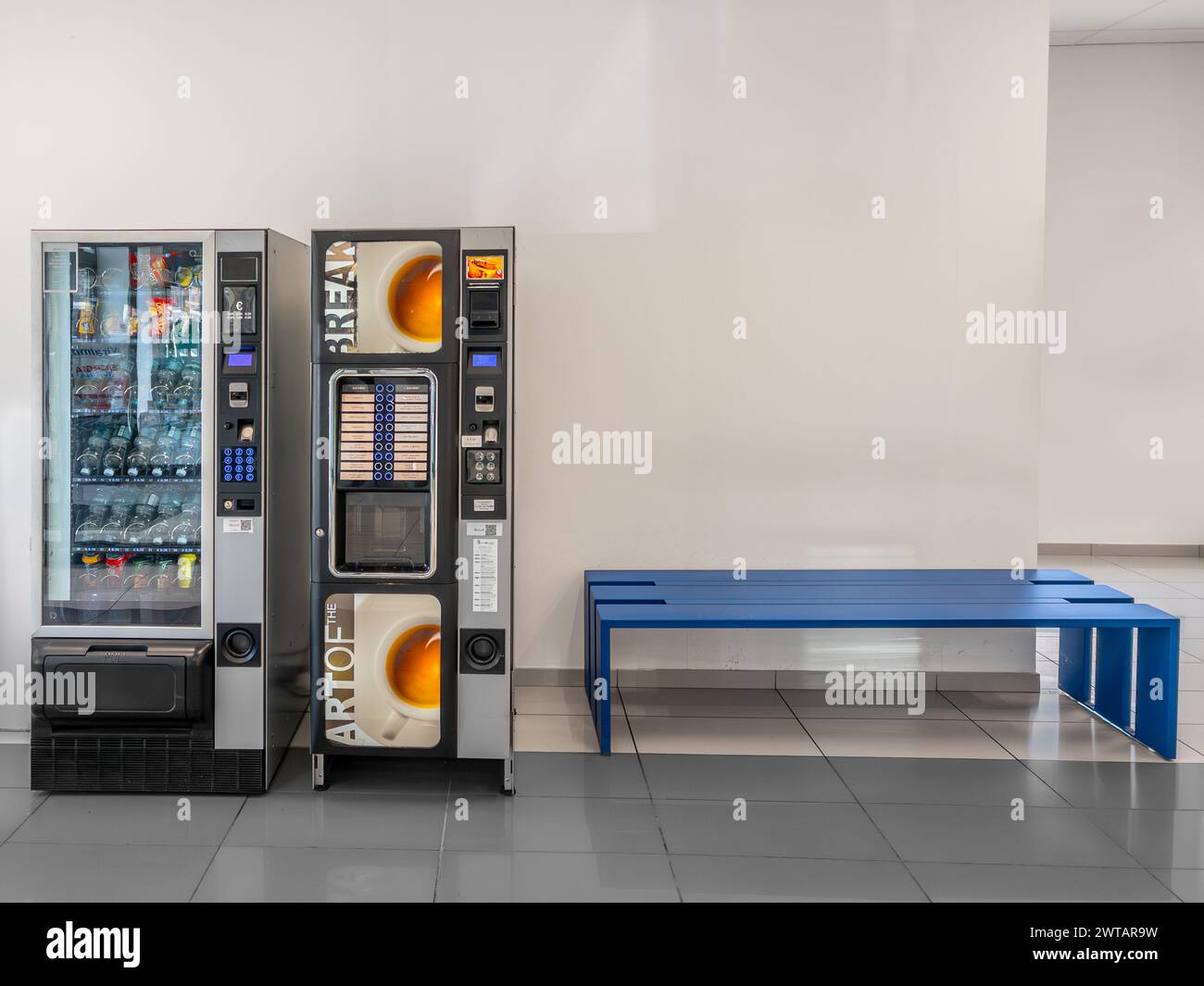 Italy - March 07, 2024: Automatic dispensers of soft drinks, water, snacks and coffee near blue bench in break coffee area Stock Photo