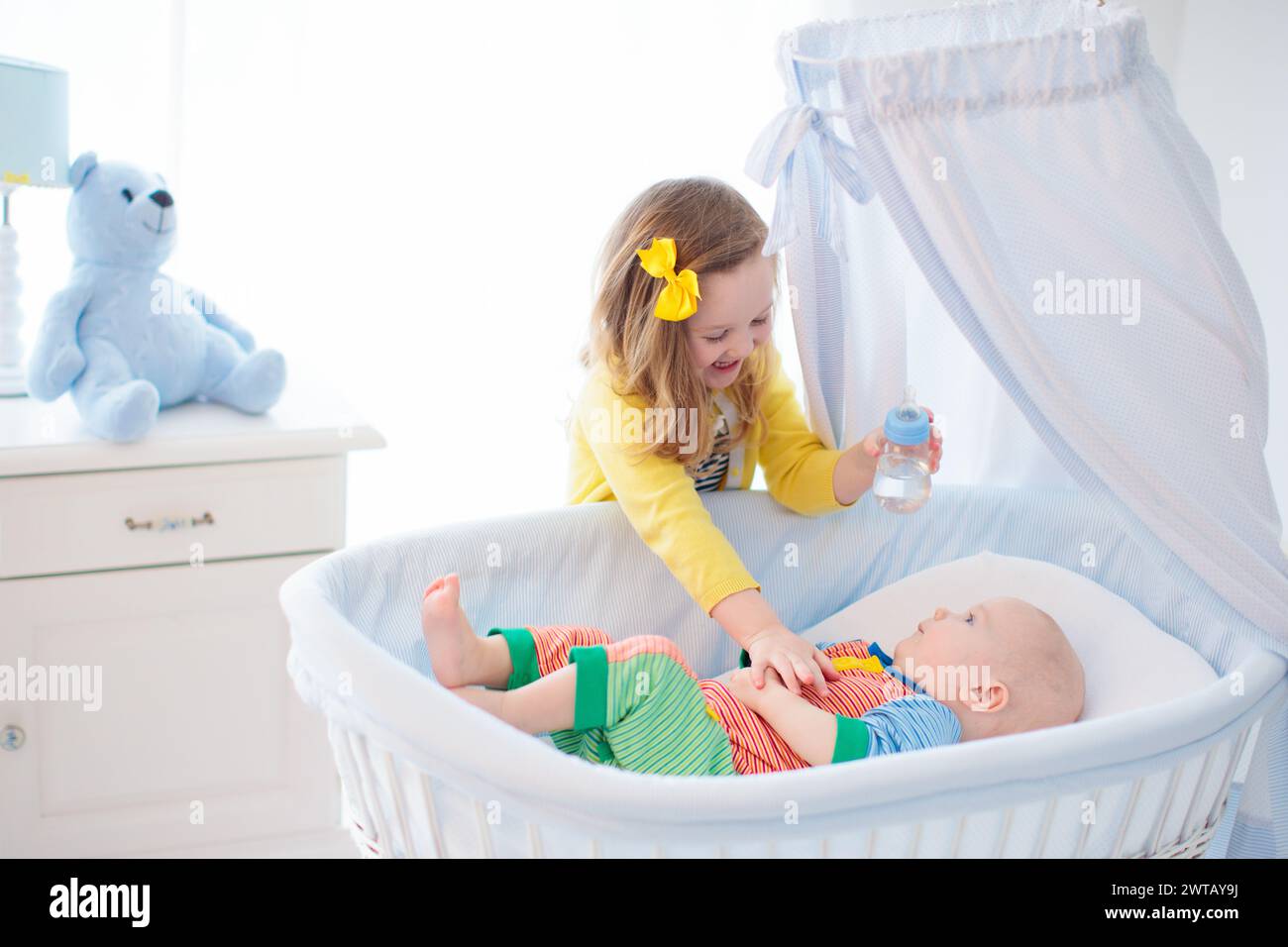 Little girl giving baby brother bottle with water or milk. Healthy
