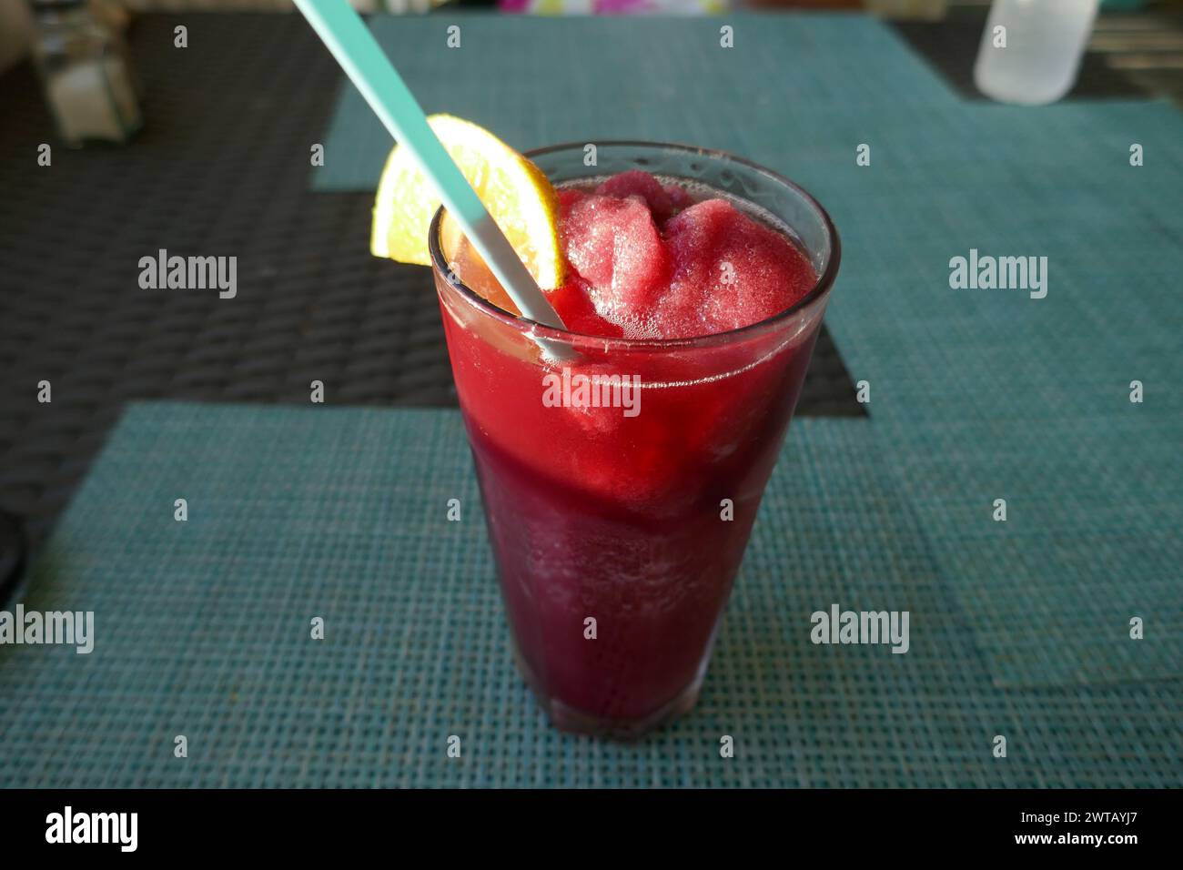 Frozen tropical drink with orange slice and drinking straw on table of outdoor restaurant Stock Photo