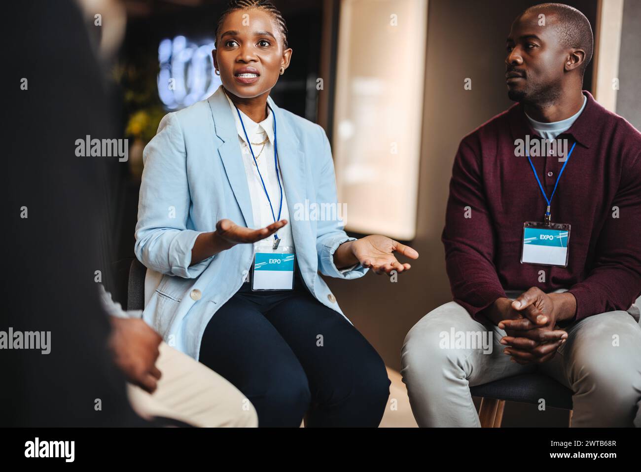 Two engaged professionals are having a focused discussion while sitting together at a business expo. Business people showing collaboration, networking Stock Photo