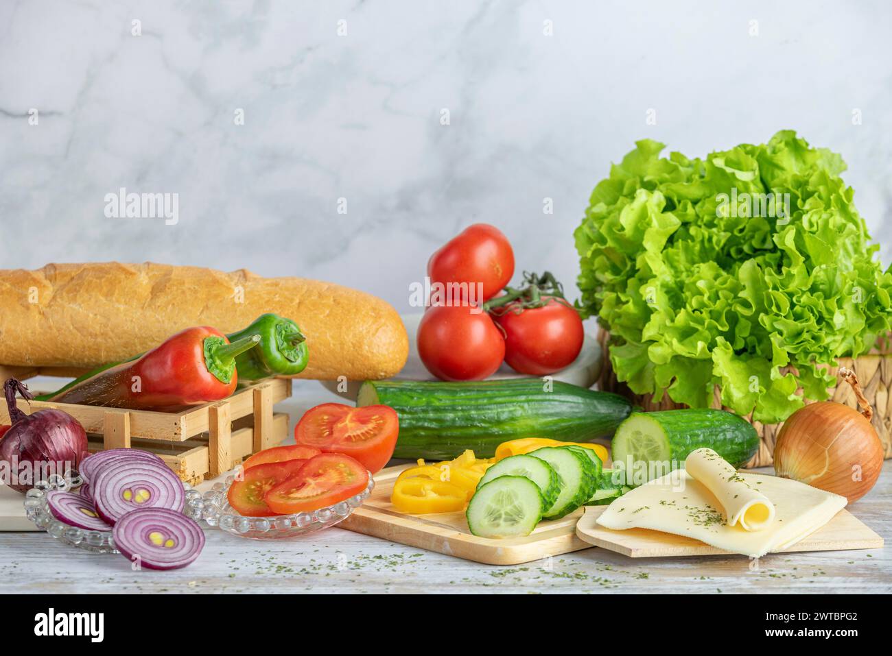 Colourful peppers, tomatoes and cucumber, some sliced, salad and cheese slices next to a baguette on a table, copy room Stock Photo