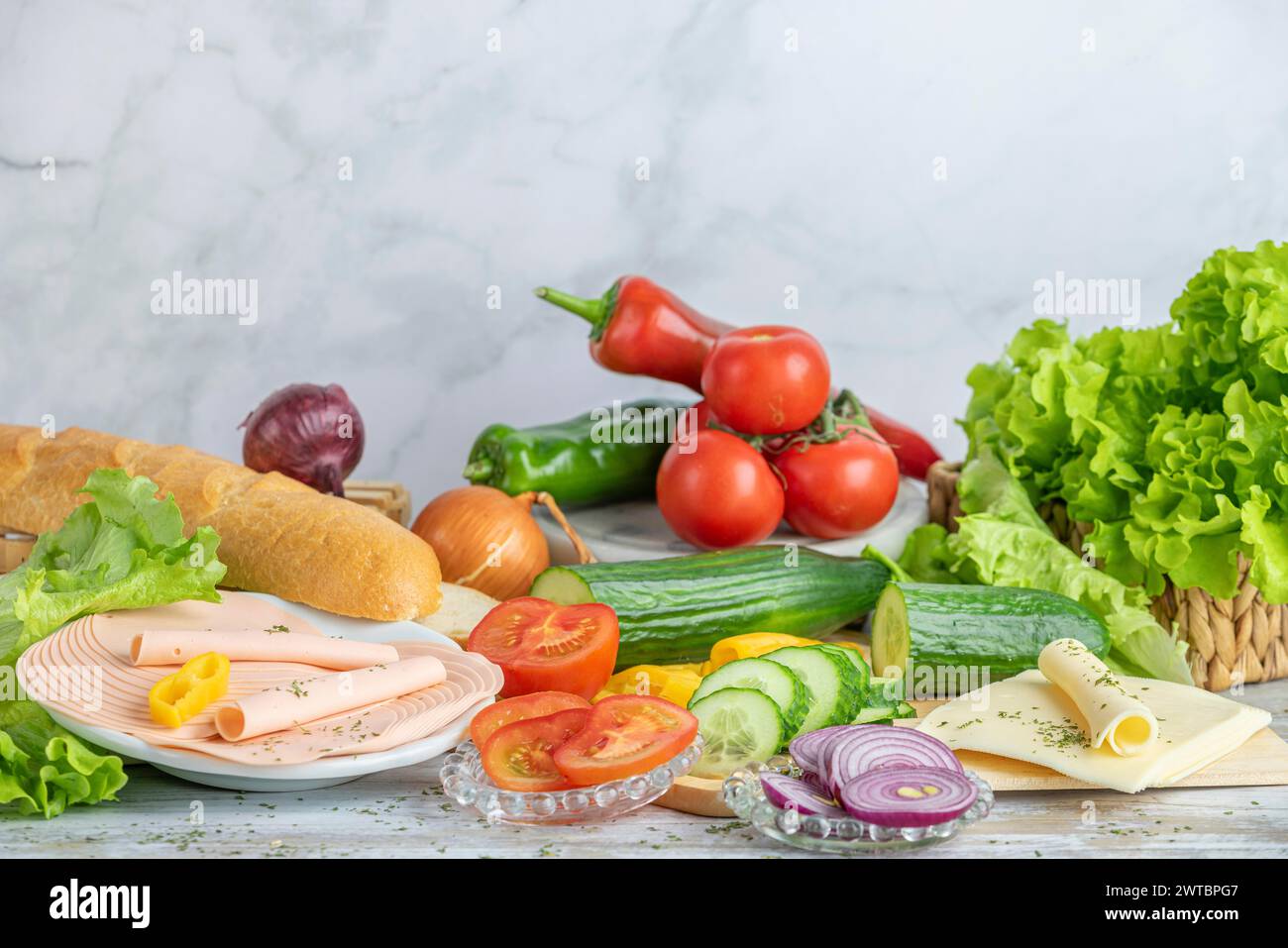 Colourful peppers, tomatoes and cucumber, some sliced, salad, cheese slices and sausage next to a baguette on a table, copy room Stock Photo