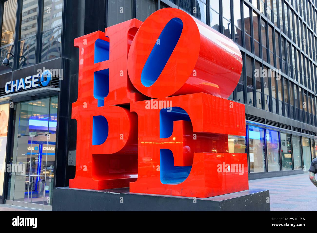 The red HOPE sculpture in front of a building with a clear blue sky in the background, on the East River, Manhattan, Brooklyn, New York City, New Stock Photo